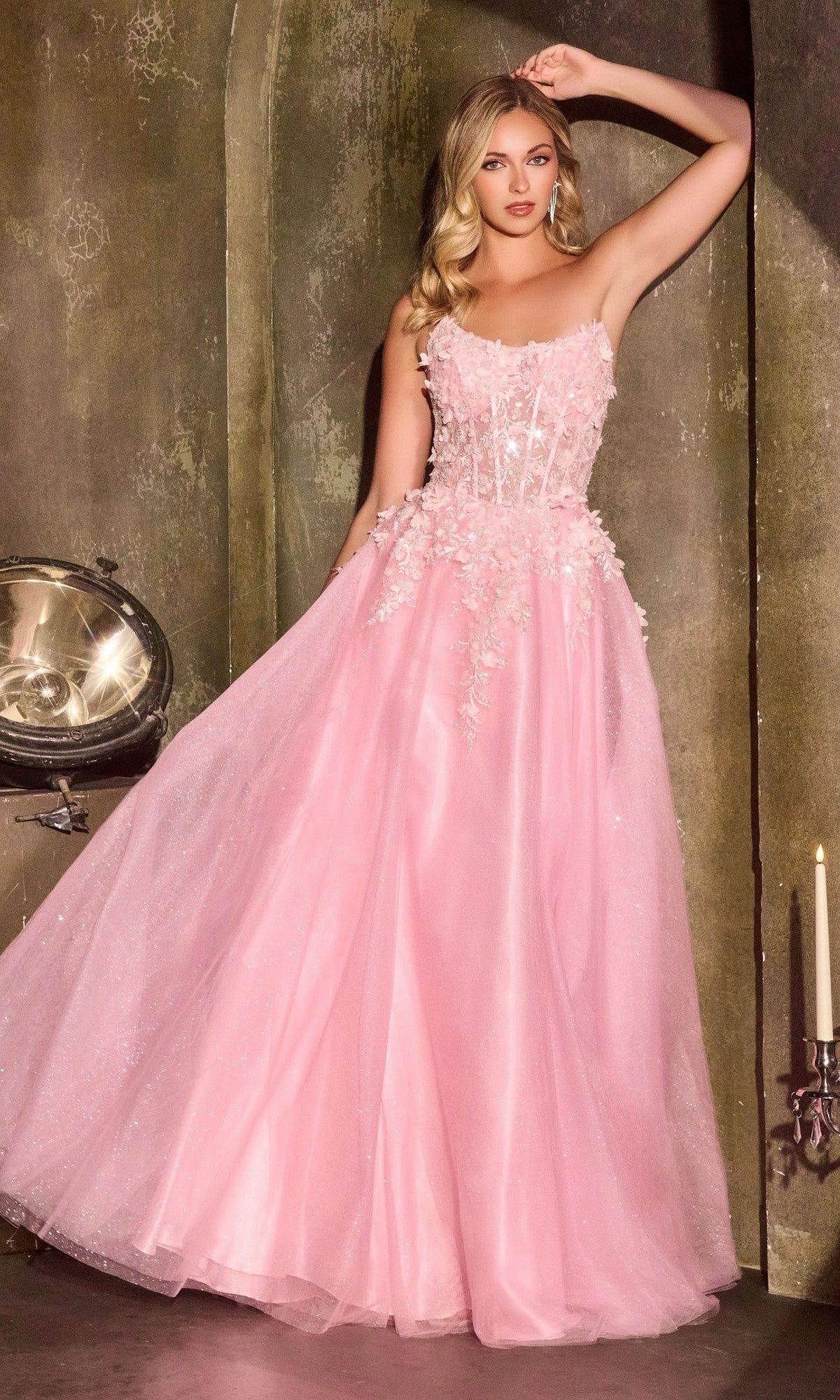 A woman in the pink Ladivine C174 Long Prom Dress, featuring a strapless design, 3D floral embroidery, and a sheer corset bodice, stands against a textured wall with one arm raised above her head.